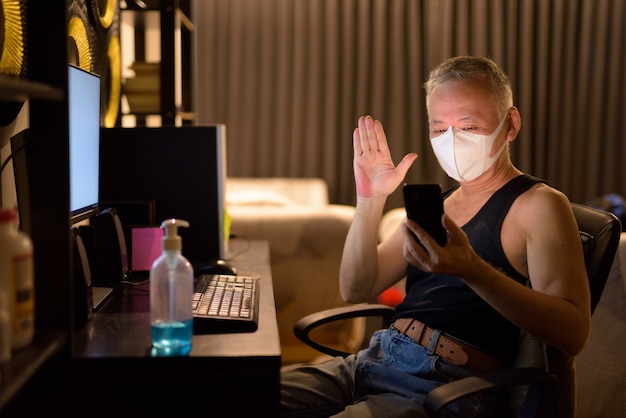 Premium Photo Mature Japanese Man With Mask Video Calling With Phone While Working Overtime At Home