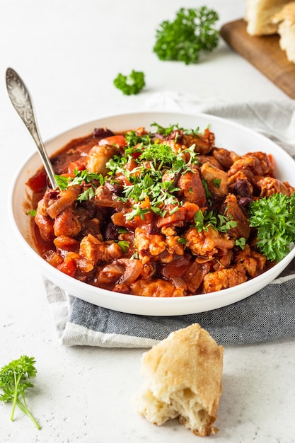 Meat stew with red beans, bell pepper and onion in tomato sauce in a white plate over light grey slate Premium Photo
