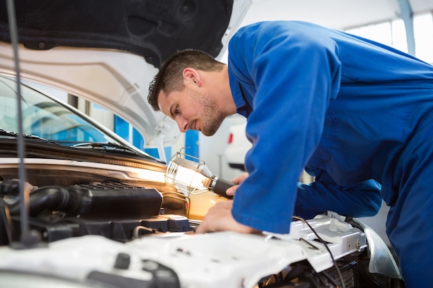 Premium Photo | Mechanic examining under hood of car with torch