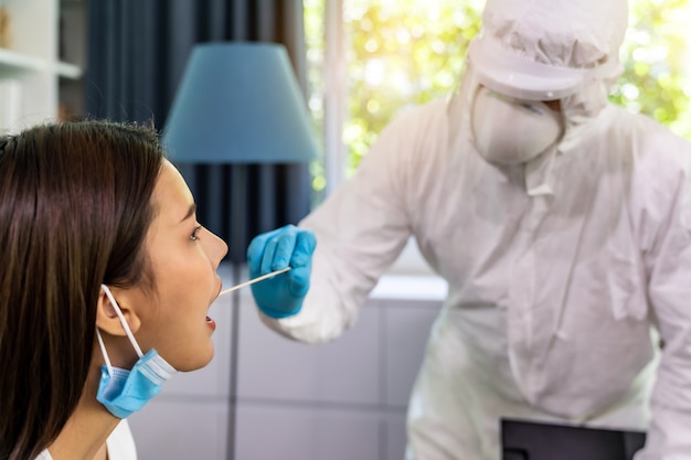 Medical staff with ppe suit test coronavirus covid-19 to asian woman by throat swab at home. new normal healthcare service at home and medical delivery concept. Premium Photo