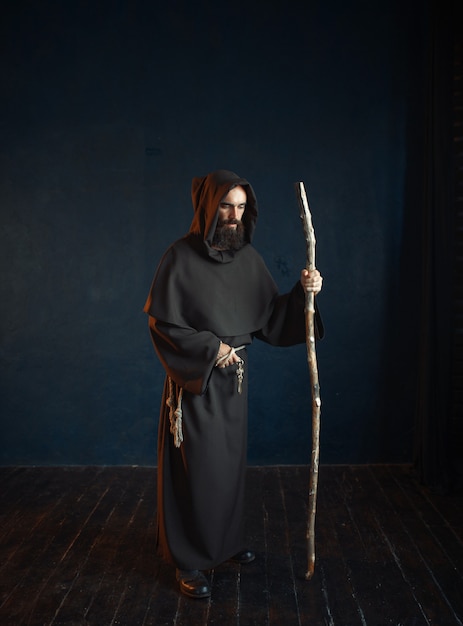 フード付きの黒いローブを着た中世の僧侶は 棒 宗教にかかっています 暗い岬の神秘的な修道士 プレミアム写真