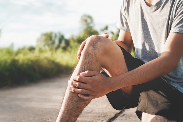 運動で負傷した男性 彼の手を使って公園で膝を抱える プレミアム写真