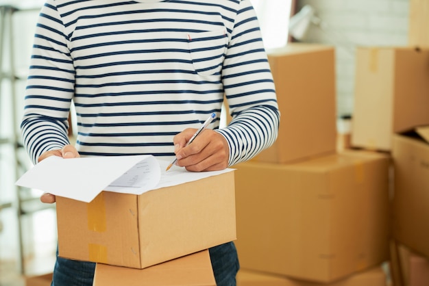 Mid-section of man in striped long sleeve shirt filling out the form on the box Free Photo