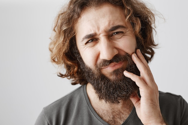 中東のひげを生やした男が頬に触れて痛みから顔をしかめ 歯痛を抱えている 無料の写真