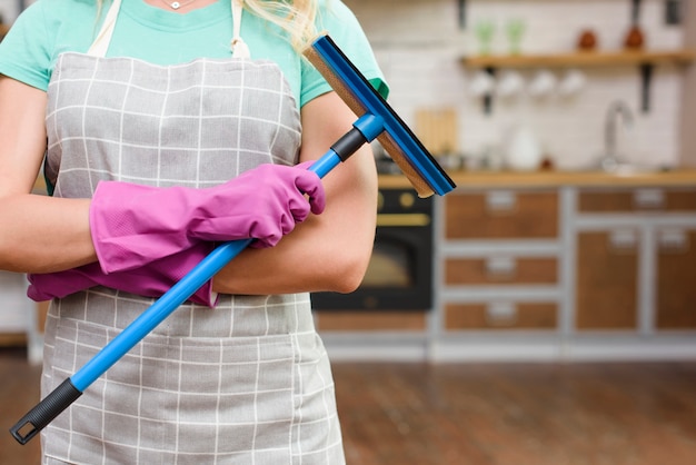 Midsection of a woman wearing apron holding plastic wiper standing in kitchen Free Photo