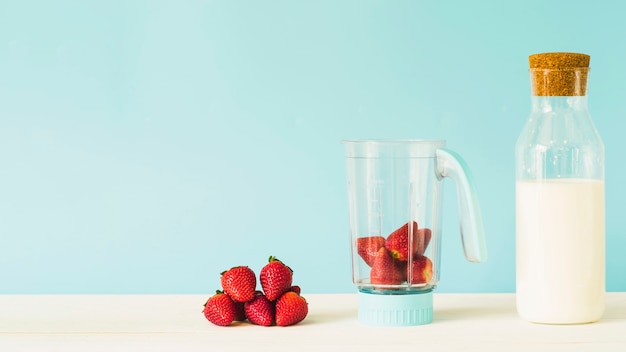 Milk bottle near strawberry in blender on wooden table Free Photo