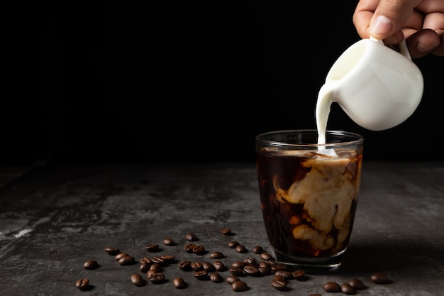 Milk pouring into iced black coffee on table Free Photo