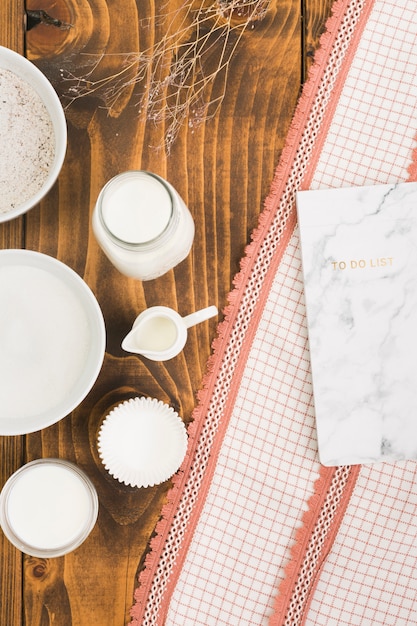 Milk; sugar; flour and cake mold with to do list on textured fabric over wooden textured table Free Photo