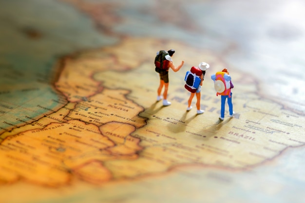 Minature people: traveling with a backpack standing on world map. Premium Photo