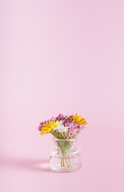 ピンクの背景に野花が付いたミニチュアガラス瓶コピースペース3月8日 イースター 母の日縦形式おめでとうございます プレミアム写真