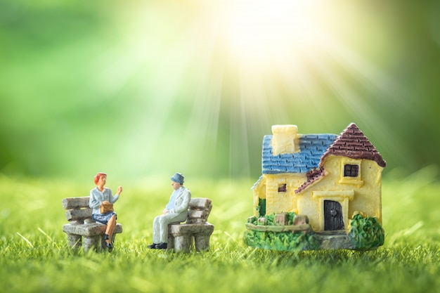 Miniature people: happy senior couple sitting in front of nursing home in a garden. Premium Photo
