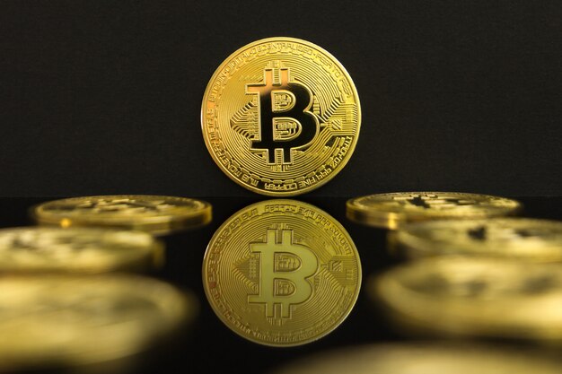 A mirror reflection of a golden btc coins. the coin of bitcoin is on a black table and black backgro