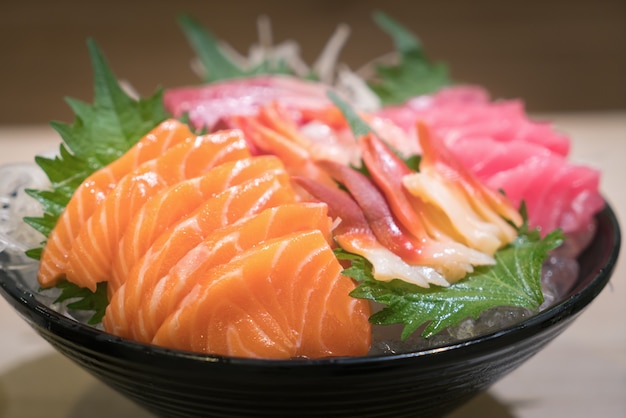 Premium Photo | Mixed sliced fish sashimi on ice in black bowl.