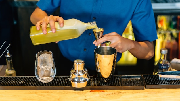 Mixologist making yuzu cocktail with shaker, double size jiggers and drinking glass Premium Photo