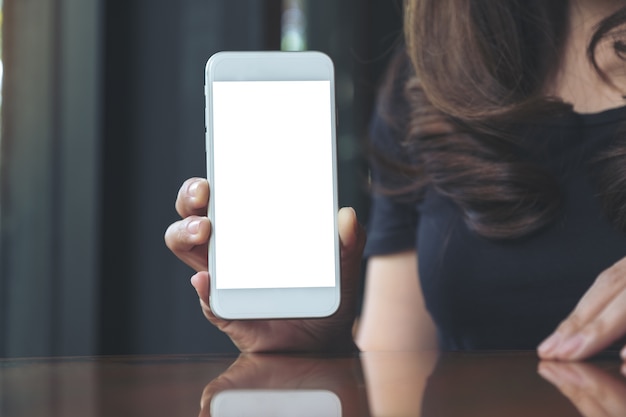 Download Premium Photo Mockup Image Of A Woman Holding And Showing White Mobile Phone With Blank Screen In Cafe PSD Mockup Templates