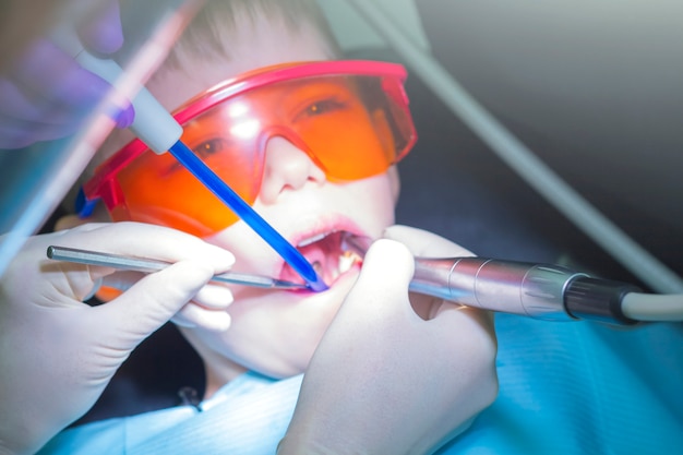 子供のための現代の虫歯治療 子供の歯科 保護用のオレンジ色のメガネの少年 プロセス治療の根管または虫歯 歯のクリーニングと予防 プレミアム写真