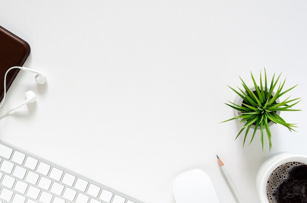 Modern workplace with wireless keyboard and mouse, a cup of coffee, smartphone with earphones, pencil and tillandsia air plant on white background. top view, flat lay Premium Photo