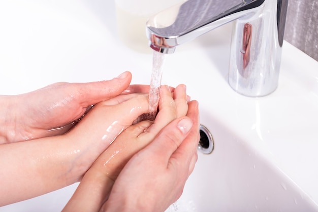 Mom washes her baby s hands under the tap in a modern bathroom Premium Photo