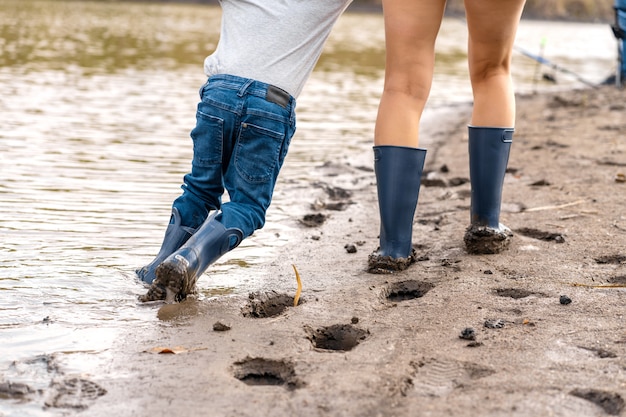 小さな息子とママはゴム長靴で湖の砂浜に沿って歩きます プレミアム写真