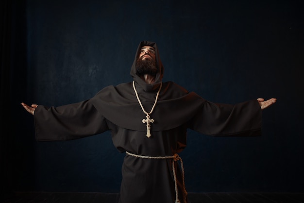 ひざまずいて祈るフード付きの黒いローブを着た僧侶 プレミアム写真