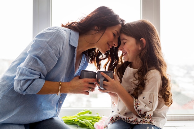 Mother and daughter drinking tea on window sill Free Photo