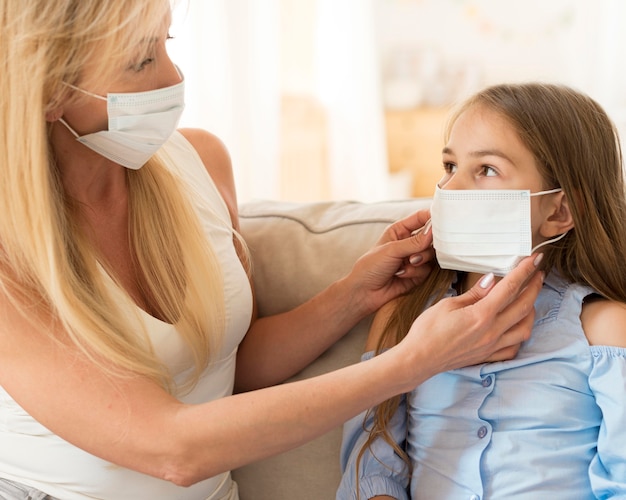 Mother helping daughter to put on medical mask on her face Free Photo