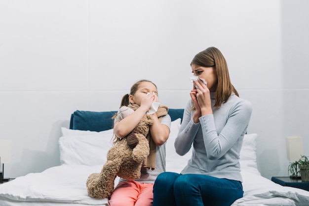 Mother looking at her daughter blowing her nose with tissue paper Free Photo