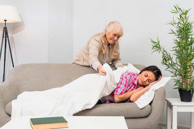 Free Photo Mother Putting Blanket Over Her Young Adult Daughter Sleeping On Sofa