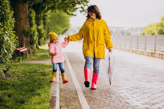 ゴム長靴を着て雨の中で公園を歩いて娘を持つ母 無料の写真