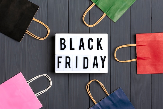 Multi-colored packaging bags, gift boxes lightbox with text black friday on dark gray surface flat lay Premium Photo