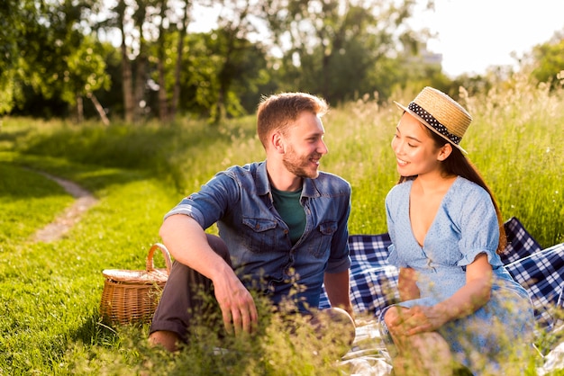 Multiracial enamored couple sitting on checkered plaid on grassy ...