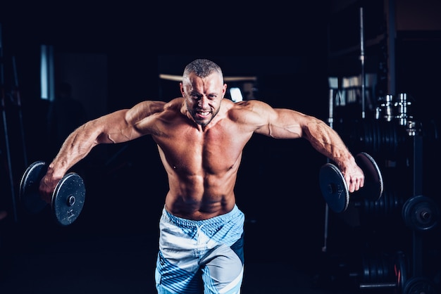 Premium Photo | Muscular man training his shoulders with dumbbells in gym