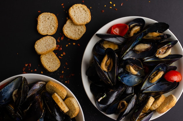 Mussel soup steamed in wine with tomatoes, hot peppers and crisp bread on black background. iitalian seafood . flat lay, top view, copy space Premium Photo