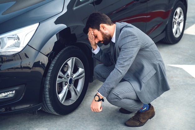 彼の車の横にしゃがんで頭を抱えている神経質なひげを生やした実業家 タイヤはパンク 今仕事に間に合うようにするにはどうすればいいですか プレミアム写真