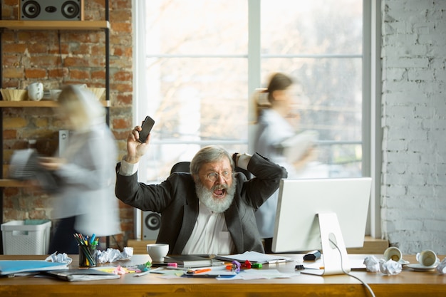 Nervous and tired boss at his workplace busy while people moving near blurred. office worker, manager working, has problems and deadline, his colleagues distracting. business, work, workload concept. Free Photo