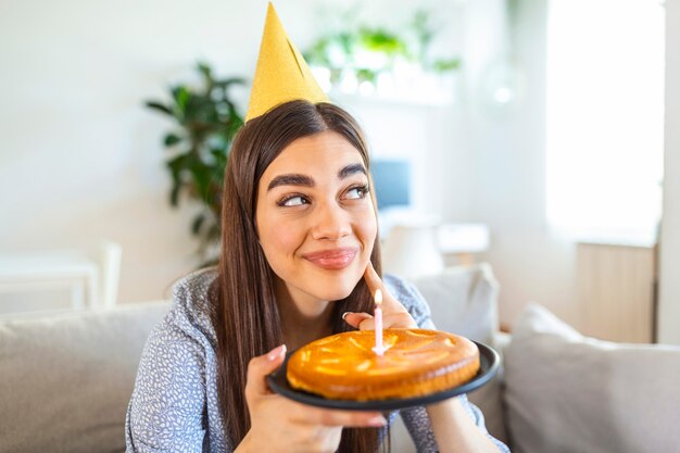 新しい通常の概念 一人で誕生日を祝う幸せな女性 ケーキを持っている若い女性 自宅での誕生日パーティー 家族のビデオ通話 人混みを避ける 家庭生活 プレミアム写真