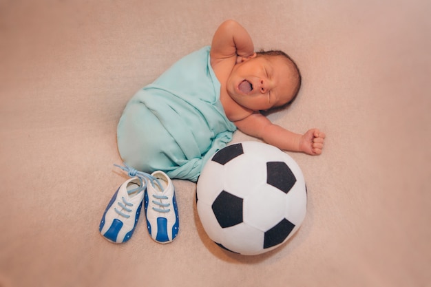 生まれたばかりの赤ちゃんとサッカーボールのパターンを持つ赤ちゃんブーティ プレミアム写真