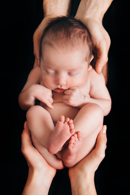 生まれたばかりの赤ちゃんが黒い背景に両親の手の上に横たわる 子宮内での赤ちゃんの模倣 プレミアム写真