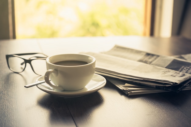Newspaper reading glasses coffee cup and mobile phone on business desk business newspaper background . Premium Photo