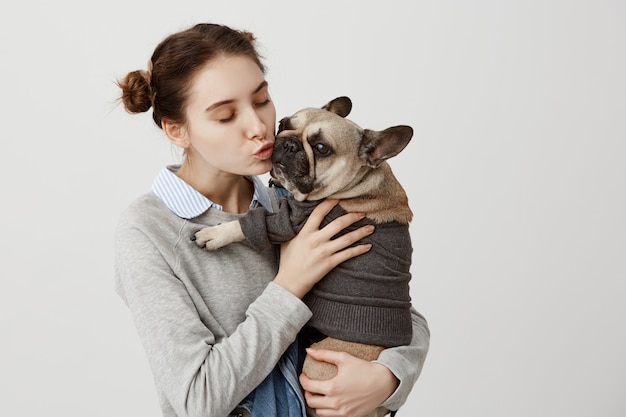 大人の女の子が優しく抱きしめながらかわいい小型犬にキスをするナイスショット 友達と一緒に時間を過ごして抱きしめる犬とその飼い主の肖像画 愛情の表示 無料の写真