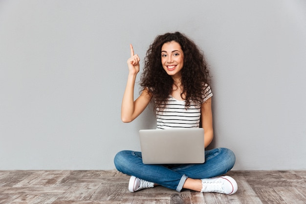 Nice woman with beautiful smile being excited to find useful information in internet via silver computer gesturing eureka sitting in lotus pose on the floor Free Photo