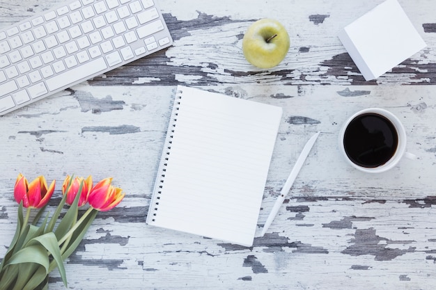 Notebook and coffee cup near keyboard and tulip flower on grungy desk Free Photo