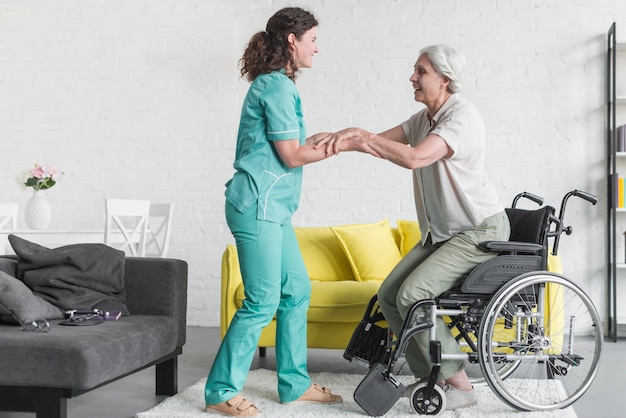 Nurse holding disabled senior woman's hand sitting on wheel chair Free Photo