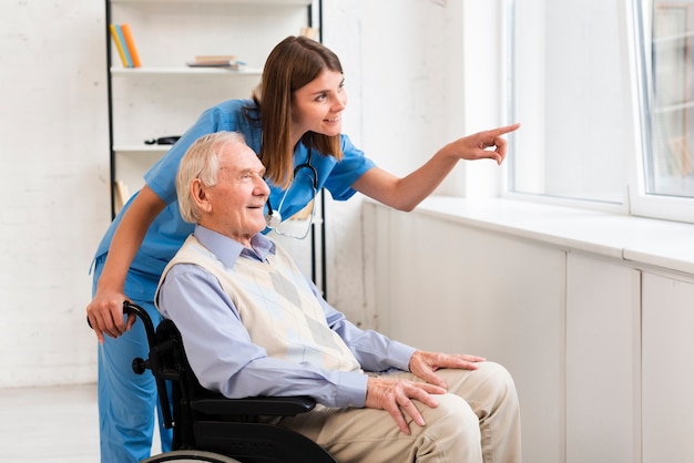 Nurse pointing to the window while talking to old man Free Photo