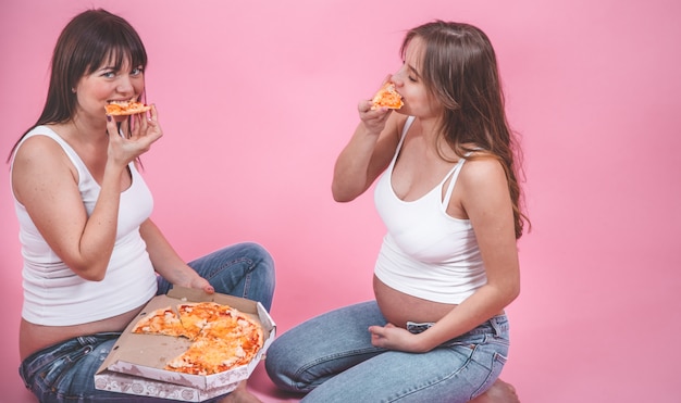 栄養の概念 ピンクの壁にピザを食べて妊娠中の女性 無料の写真