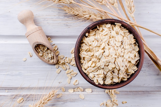 Oat flakes in ceramic bowl and wooden spoon and spikelets Premium Photo