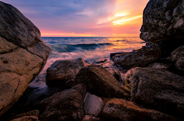 ピンクと金色の夕焼け空とロックビーチに海の水のしぶき 夏の海岸で石の上にしぶき海の波 ソフトウェーブ プレミアム写真