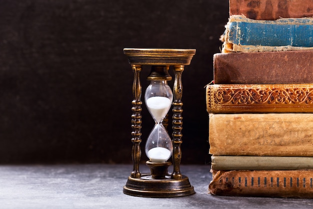 Premium Photo | Old hourglass with books on dark