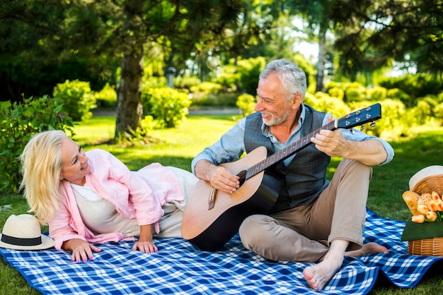 Mature Man Playing Guitar While Sitting With Wife On Sofa