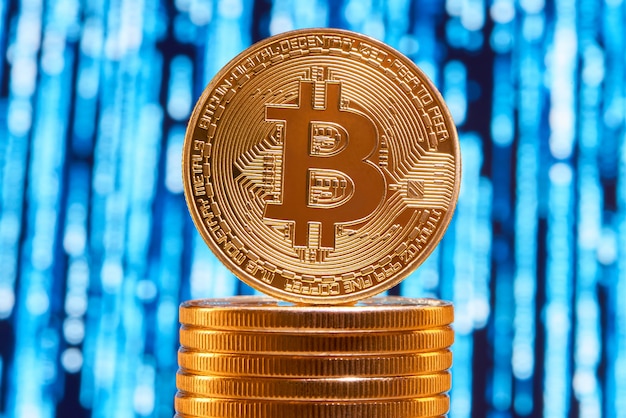 One bitcoin on edge placed on stack of golden bitcoins with blurred blue circuit on background. Premium Photo
